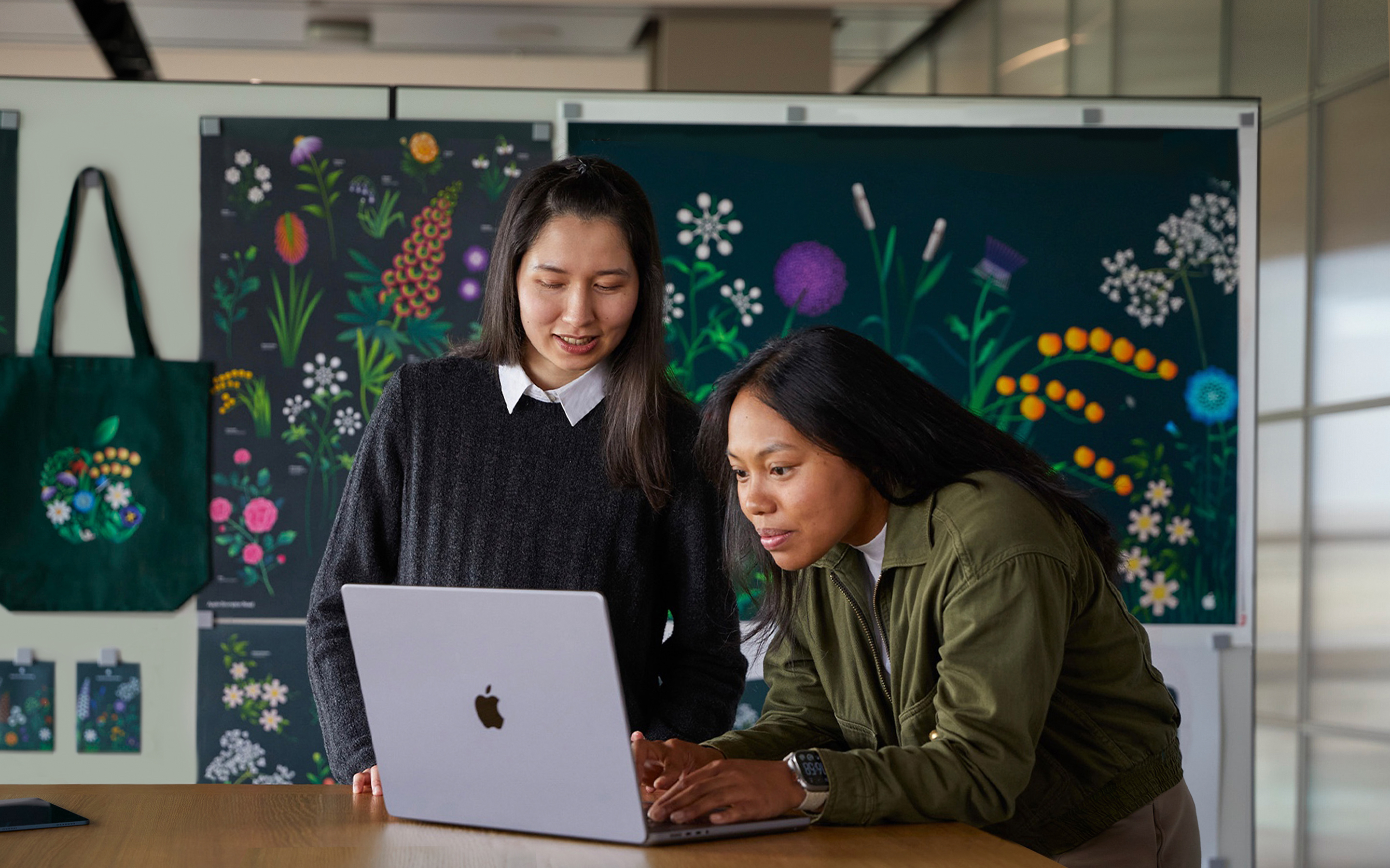 Dos personas del equipo de Marketing de Apple trabajan juntos en una MacBook delante de carteles diseñados por su equipo.