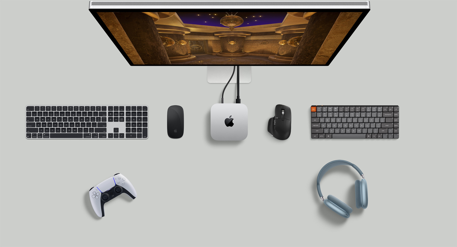 Pohled shora na Mac mini v sestavě se Studio Displayem, bezdrátovými klávesnicemi, bezdrátovými myšmi, herním ovladačem a AirPody Max