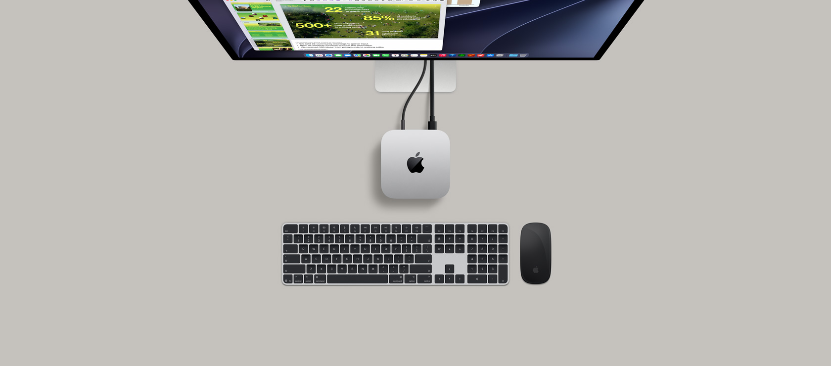 Pohled shora na Mac mini, stříbrný hliník, zakulacené rohy, uprostřed lesklé černé logo Apple, připojení kabelem, nahoře je částečně vidět Studio Display, otevřené AirPody 4, vzorky barev Pantone, červená klávesnice a myš Logitech