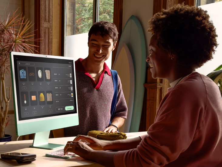 شخصان في غرفة مضاءة جيداً، أحدهما يتحقق من طلب على iMac أخضر بشريحة M4 .