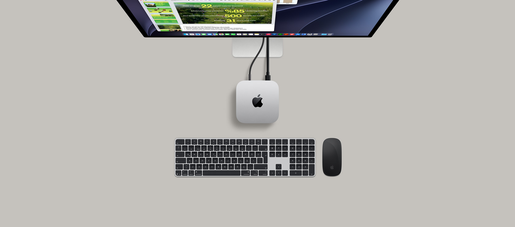 Mac mini, üstten görünüm, gümüş rengi alüminyum, yuvarlatılmış köşeler, ortalanmış parlak siyah Apple logosu, kabloyla bağlı, üst kısımda ekranda Takvim uygulamasının, Keynote sunumunun ve çubuk grafiğinin açık olduğu Studio Display kısmen görünüyor, Sayısal Tuş Takımlı Magic Keyboard, Mac mini’nin altında Magic Mouse