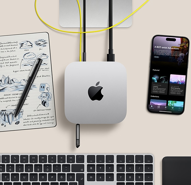 Mac mini, üstten görünüm, gümüş rengi alüminyum, yuvarlatılmış köşeler, ortalanmış parlak siyah Apple logosu, kabloyla bağlı, öndeki USB-C bağlantı noktasına USB bellek takılı, Studio Display standının kısmi görünümü, iPhone, Magic Trackpad, Touch ID özellikli Magic Keyboard, kalem, elektronik mürekkep tabanlı eskiz tableti