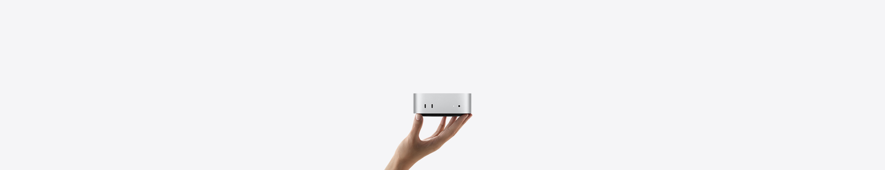 向上展開的手，指尖上平衡地立著一部銀色 Mac mini，機身朝前，正面秀出兩個 Thunderbolt 埠、狀態指示燈與耳機插孔、底端收窄設計的黑色底座、平坦的頂端、圓角側邊與平直的機身邊緣