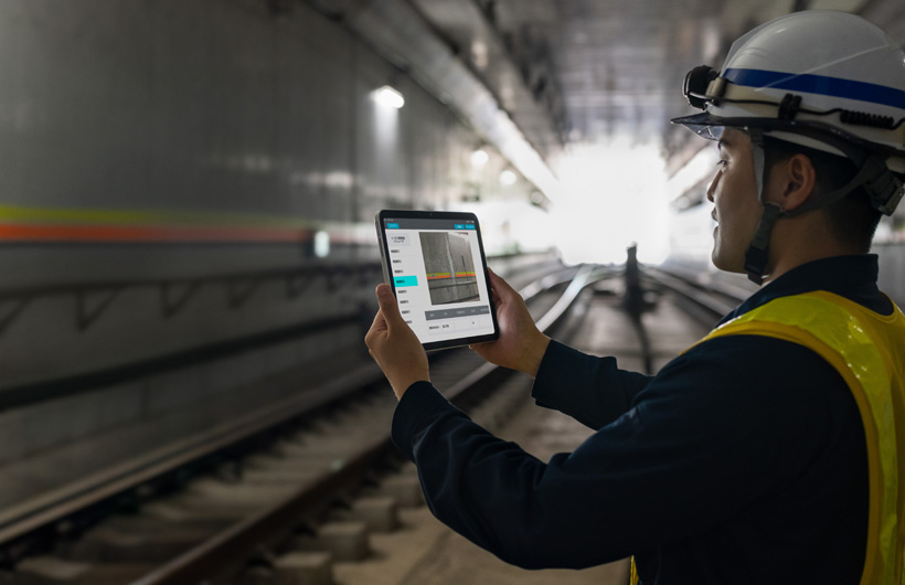Un technicien de maintenance dans les tunnels du métro de Tokyo tient un iPad pour prendre les rails en photo tandis qu’un collègue l’observe.