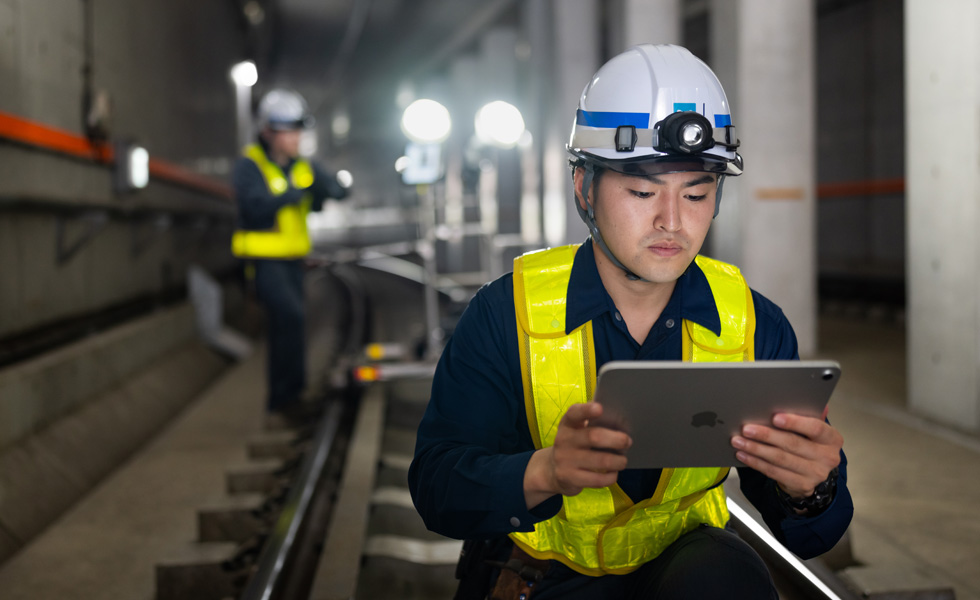 Un technicien portant un gilet de sécurité et un casque de protection regarde un iPad alors qu’il effectue des travaux de maintenance dans les tunnels du métro de Tokyo.