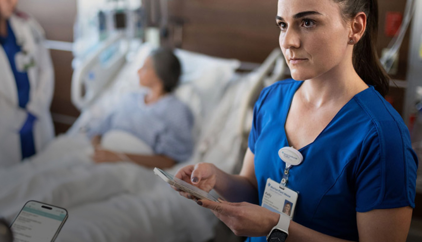 Eine Pflegekraft schreibt auf ihrem iPhone eine Textnachricht, während eine andere Medizinerin mit einer Patientin spricht.