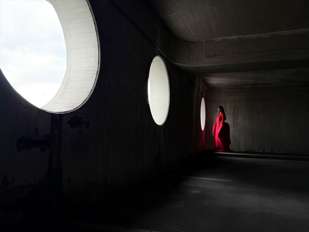 赤いロングドレスを着た女性が、誰もいない部屋に立っている画像。写真アプリの焦点距離が切り替わり、プロのカメラシステムの機能を紹介している。焦点距離「28mm」の画像が表示されている