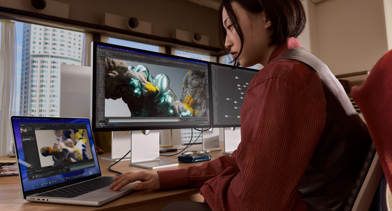 Una persona en una oficina trabaja en un portátil MacBook conectado a un monitor Studio Display XDR mediante un puerto Thunderbolt 5