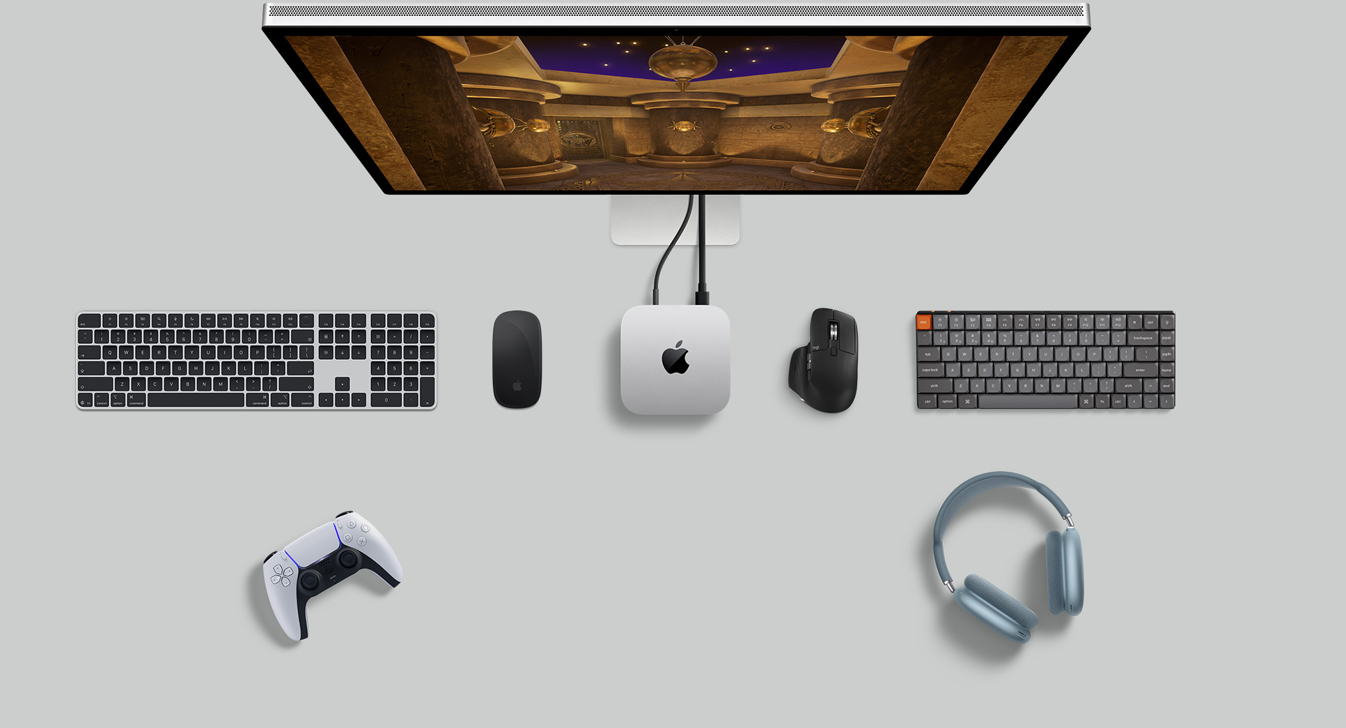 Mac mini nhìn từ trên xuống trong không gian bàn làm việc có Studio Display, bàn phím không dây, chuột không dây, tay cầm chơi game và AirPods Max